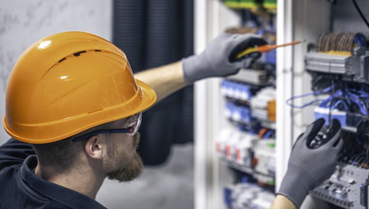 A male electrician works in a switchboard with an electrical connecting cable.